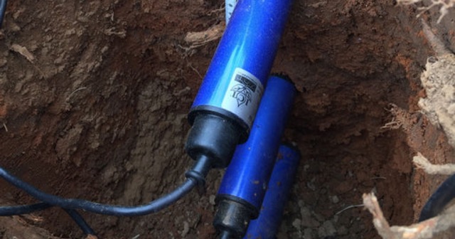 Installed soil moisture sensors in a grow bag, with its data cable running alongside drip irrigation lines, connected to an automated greenhouse control system.